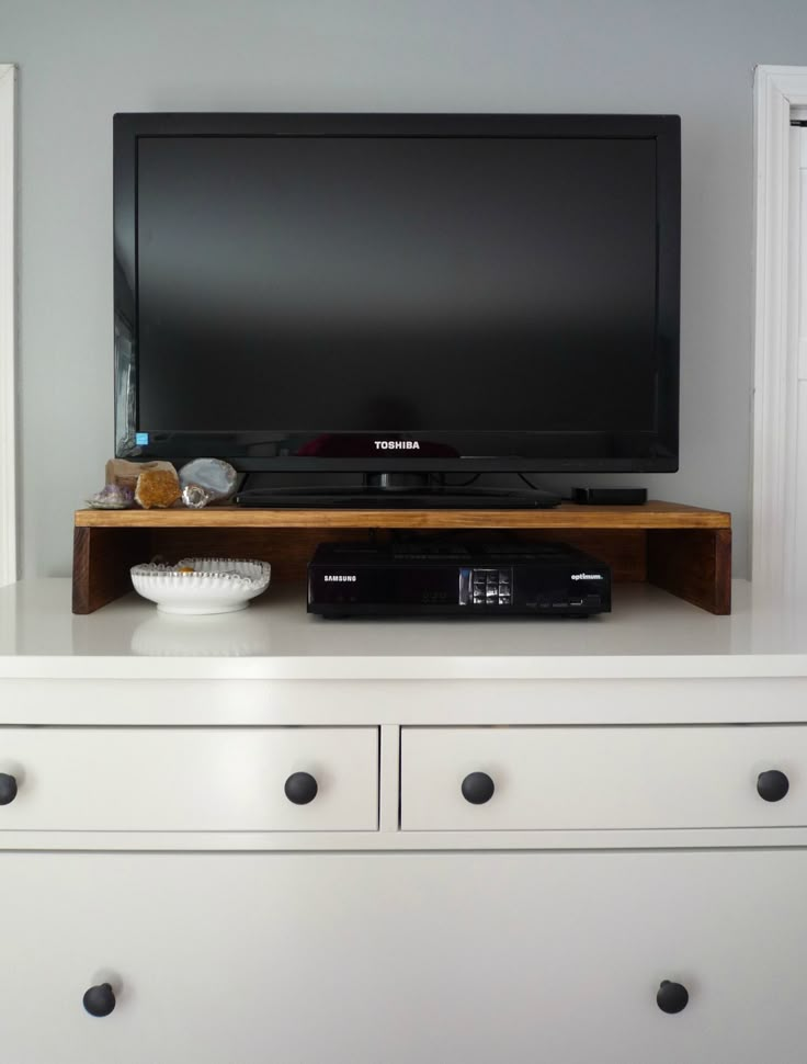 a flat screen tv sitting on top of a white dresser next to a bowl of fruit