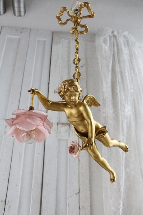 an angel figurine hanging from a chandelier with pink flowers in front of it