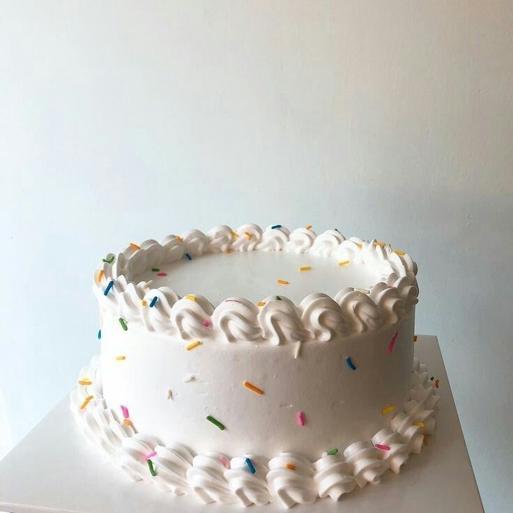 a white frosted cake with sprinkles sitting on top of a table