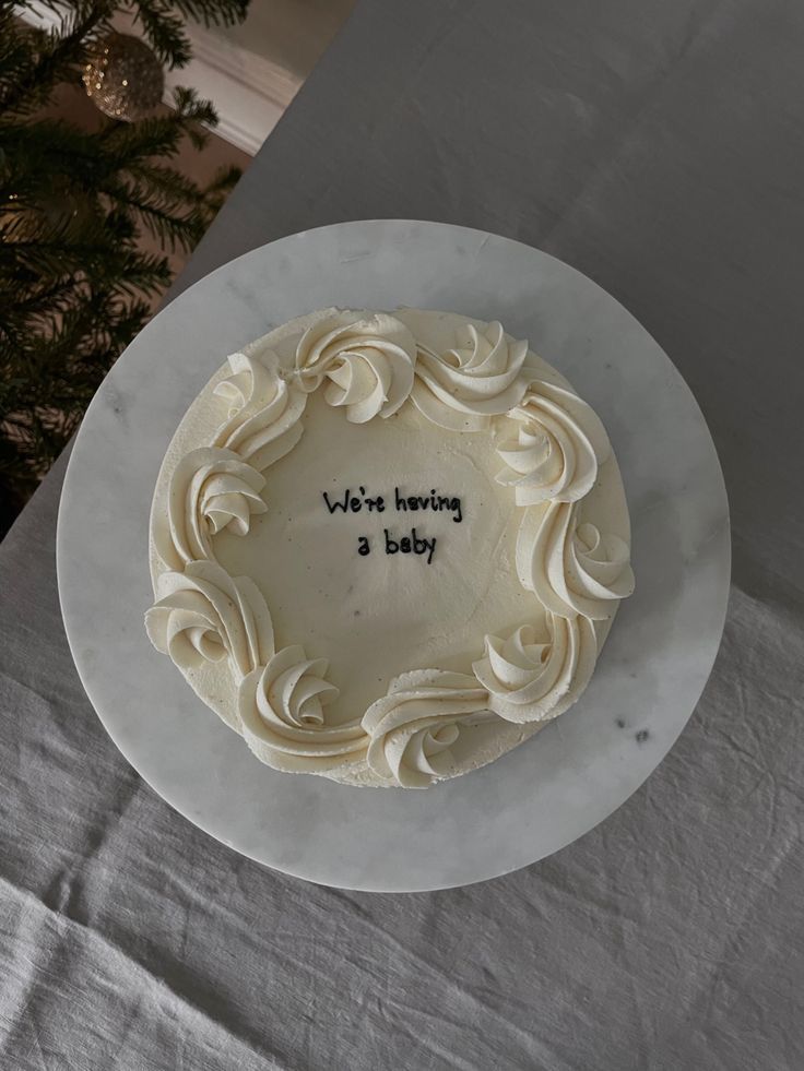 there is a white frosted cake with writing on the top and below it that says, we're having a baby