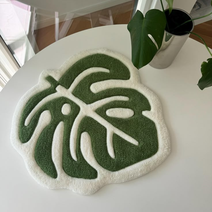 a white table topped with a green and white rug next to a potted plant