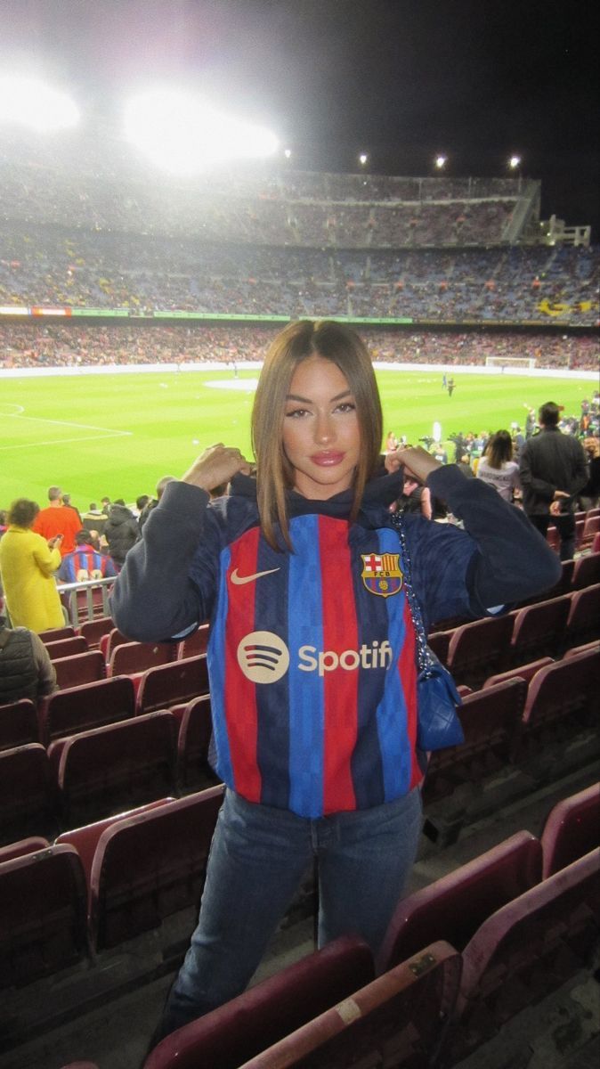 a woman standing in the stands at a soccer game wearing a blue and red jacket