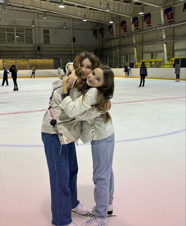 two girls hugging each other on an ice rink