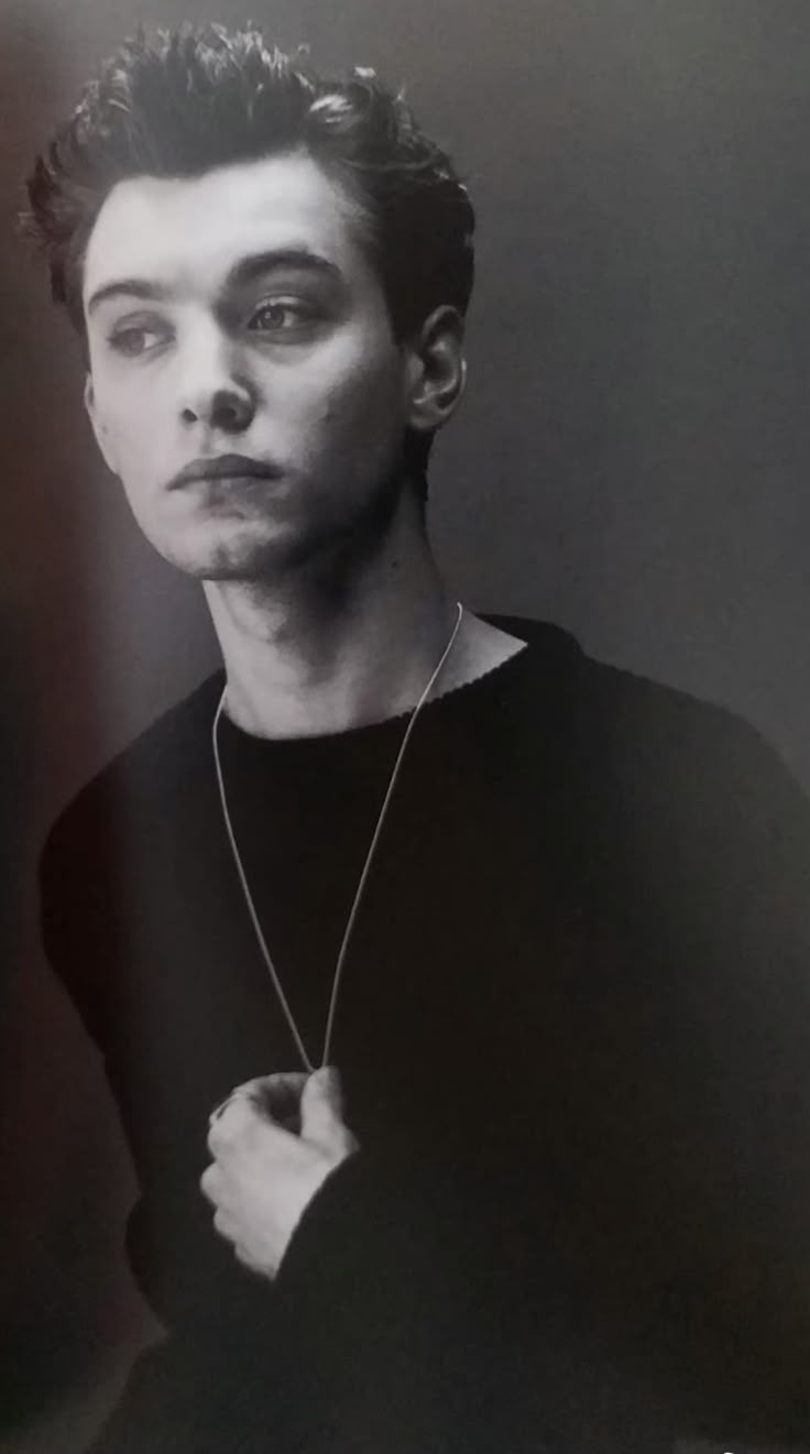 a black and white photo of a young man with his hand on his chest looking at the camera