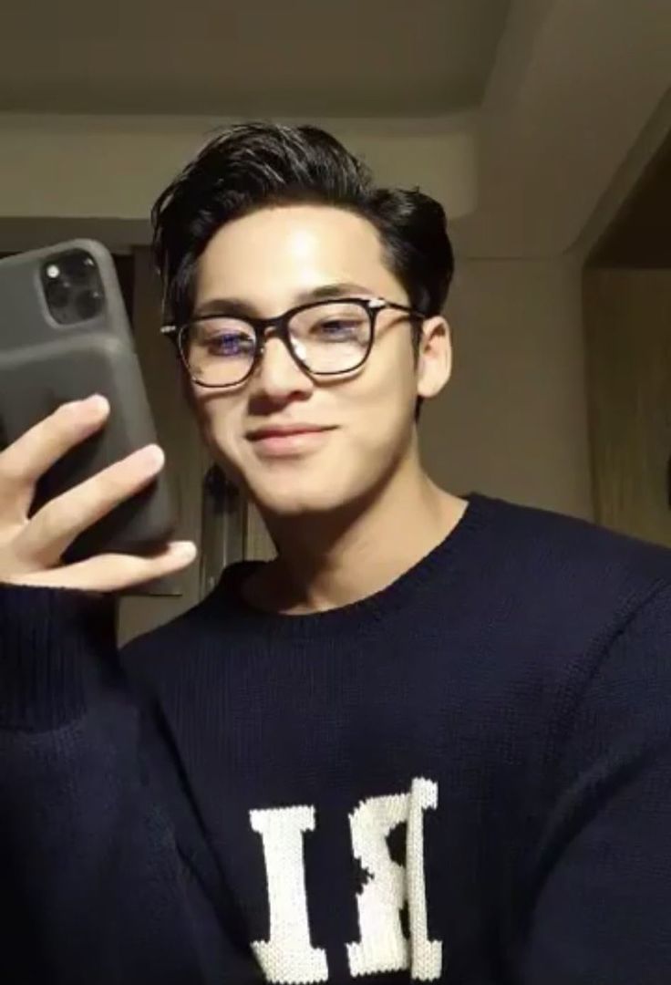 a man wearing glasses taking a selfie with his cell phone in front of him