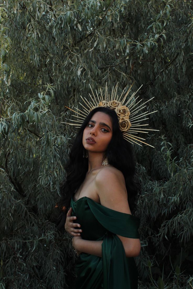 a woman in a green dress with a crown on her head standing next to trees