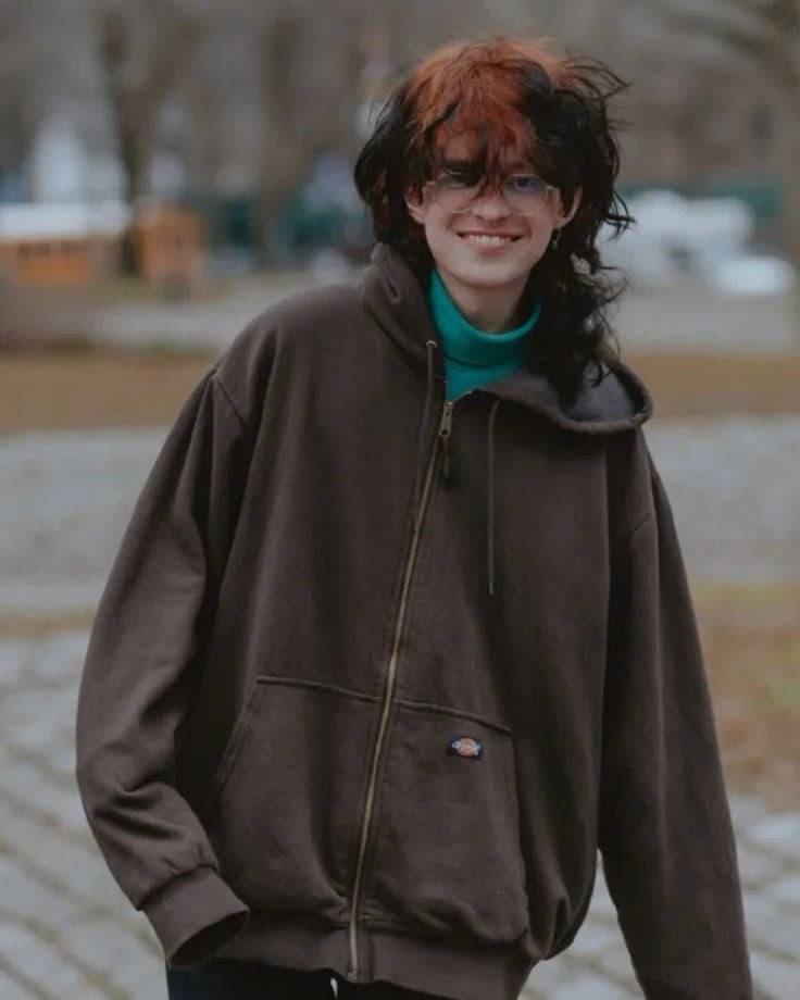 a woman with red hair and glasses standing in front of a brick walkway smiling at the camera