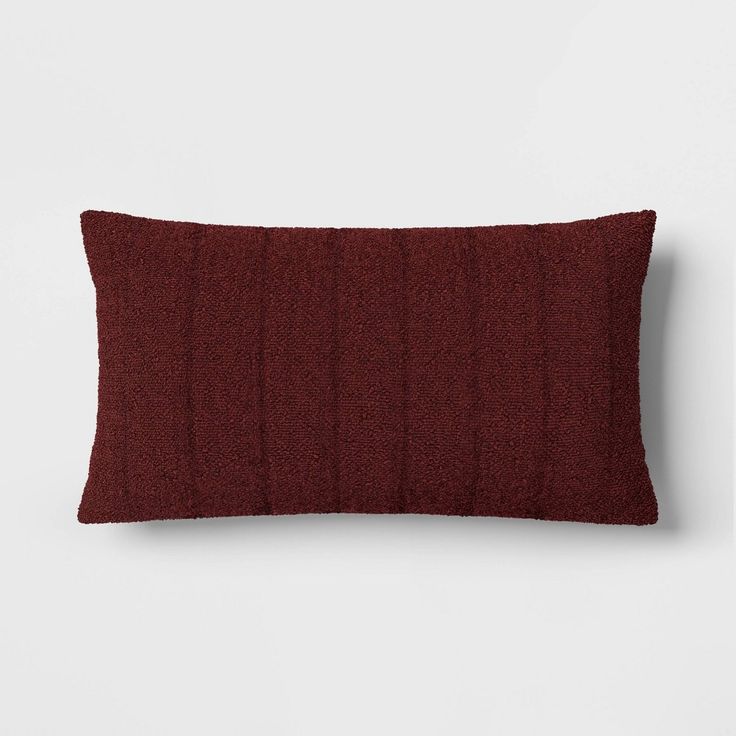 a red pillow on a white wall with a dark brown corded material behind it