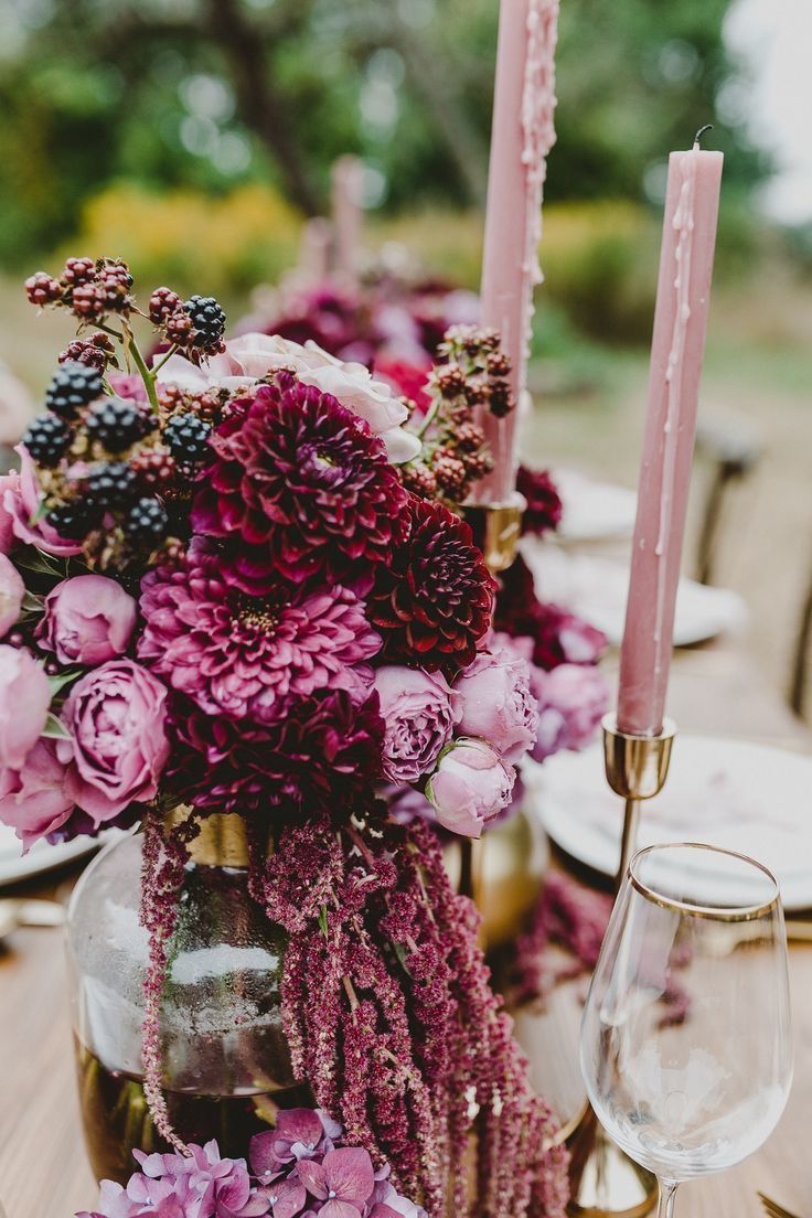 an arrangement of flowers and candles on a table with plates, wine glasses and napkins