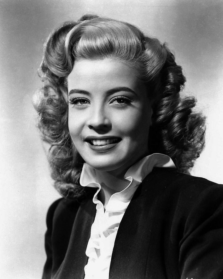 an old black and white photo of a woman with curly hair wearing a cardigan