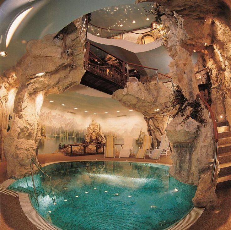 an indoor swimming pool in the middle of a room with rocks on the wall and stairs leading up to it