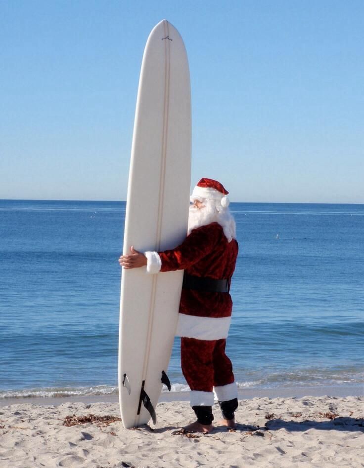 a man dressed as santa claus holding a surfboard on the beach