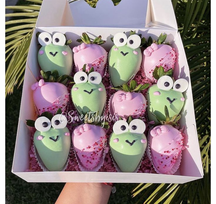 a box filled with cupcakes covered in green and pink frosting topped with googly eyes