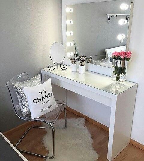 a white vanity table with a mirror and lights on it next to a flower vase