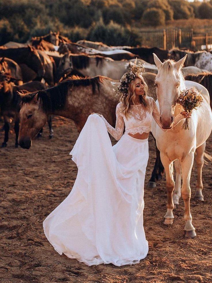 a woman in a white dress standing next to a horse and some other horses on a dirt field