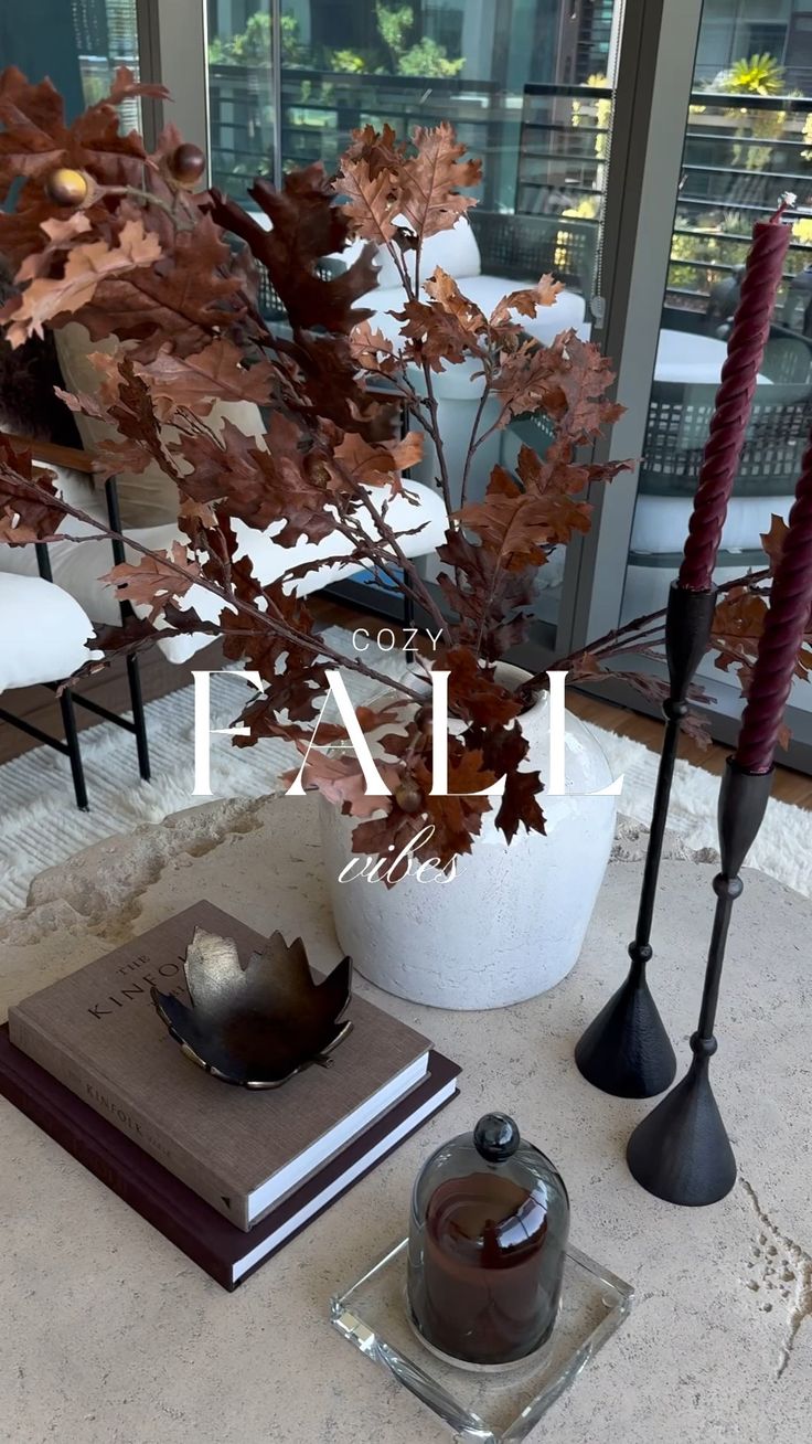 an arrangement of candles, books and vases on a table in front of a window