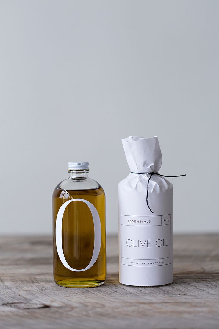 a bottle of olive oil next to a paper bag on a wooden table with a white ribbon