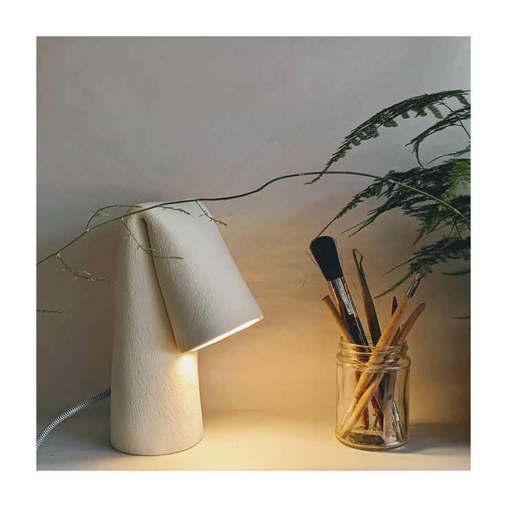 a lamp that is on top of a table next to a vase with pens and pencils in it