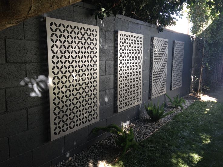 three decorative panels on the side of a wall next to a grass area and trees