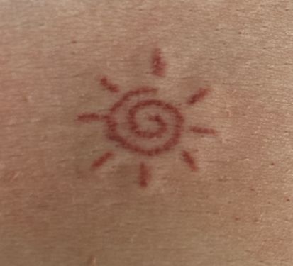 the back of a person's neck with a sun tattoo on it and red ink