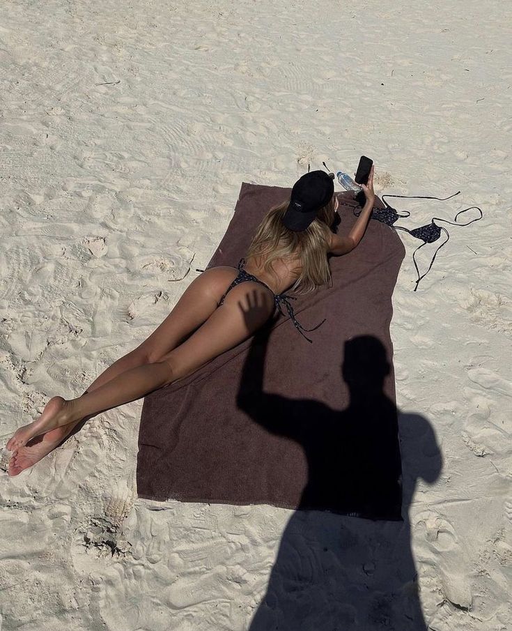 a woman laying on top of a beach next to a towel and cell phone in her hand