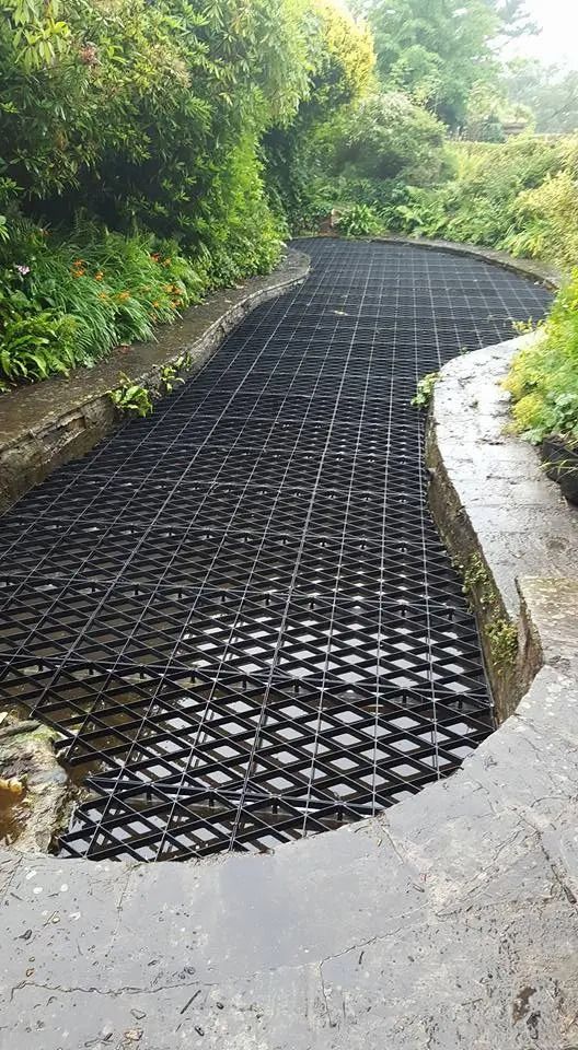 a large metal grate sitting on the side of a road next to lush green trees