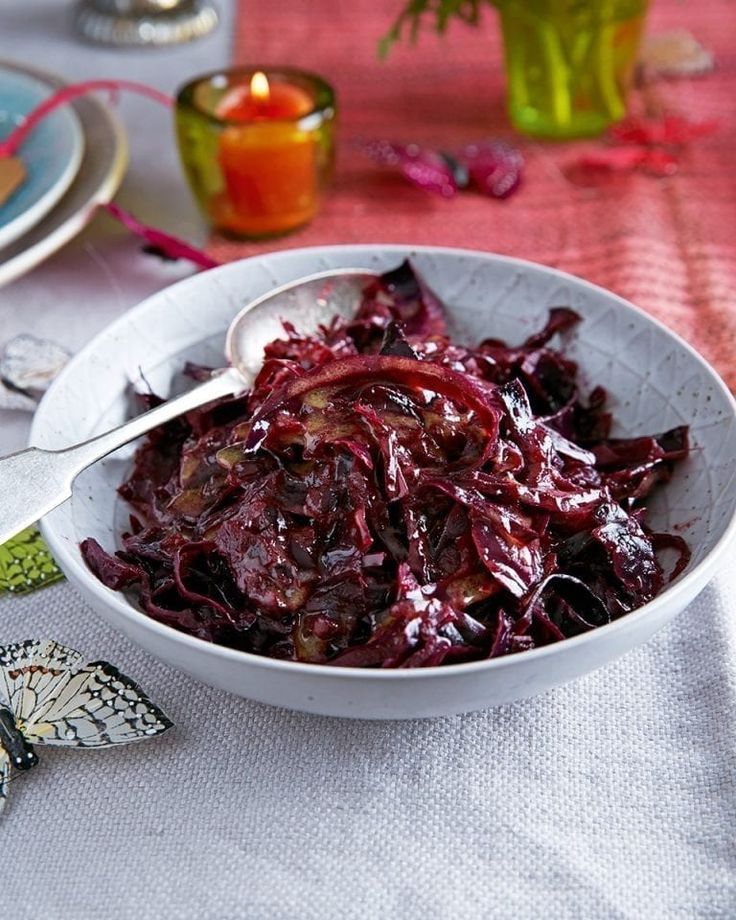 a white bowl filled with red cabbage on top of a table next to other plates