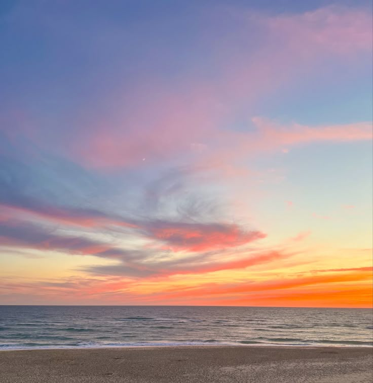 the sun is setting over the ocean with clouds in the sky and sand on the beach