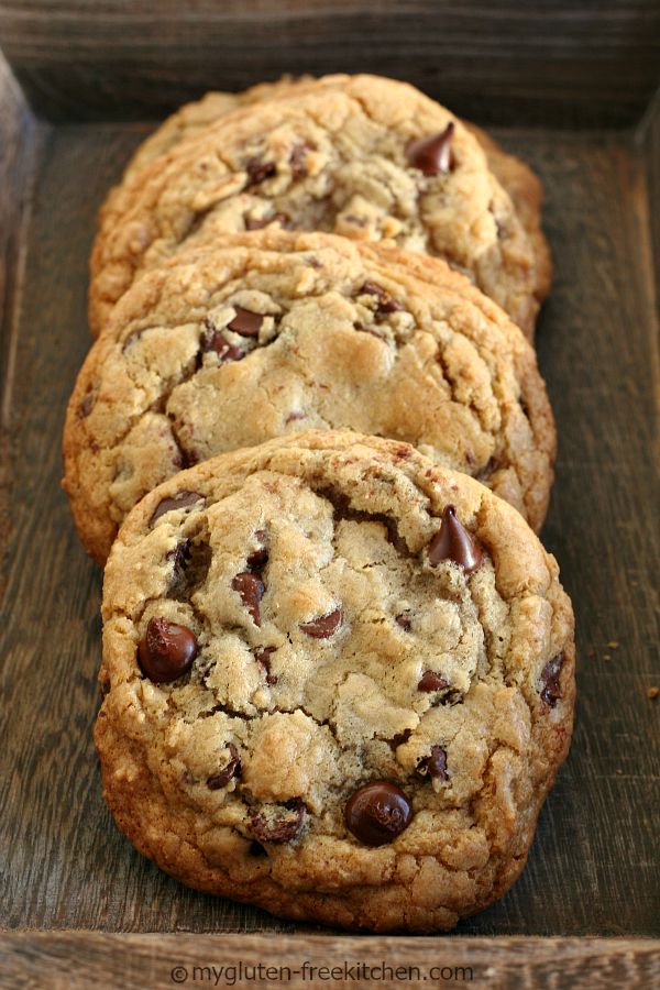 four chocolate chip cookies sitting on top of a wooden tray