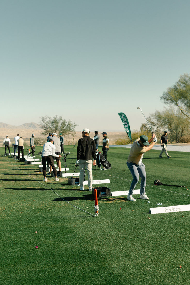 a man swinging a bat on top of a lush green field next to people playing golf