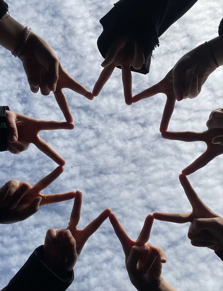 several people are holding their hands together in the shape of a star against a cloudy sky