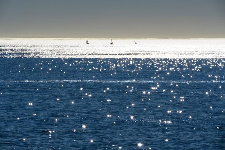 the sun shines on the water and sailboats are in the distance behind them