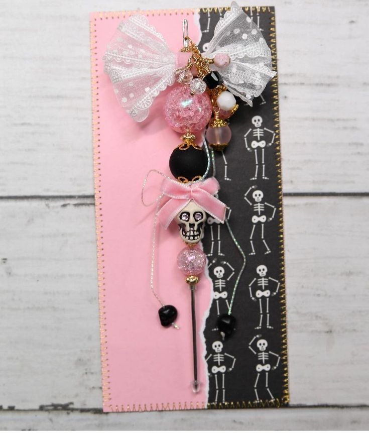 a pink and black card with a skeleton on it's head, some beads and a bow