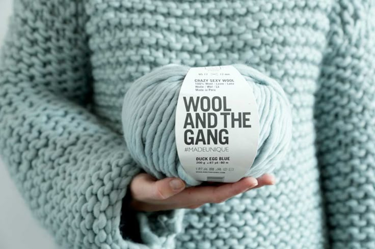 a woman holding a ball of wool and the gang yarn in her hands, against a white background