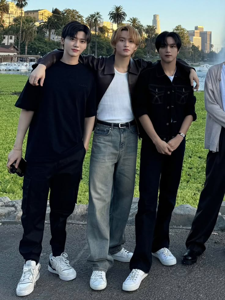 three young men standing next to each other in front of a park with palm trees