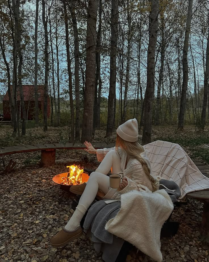 a woman sitting on a bench next to a fire pit in the middle of a forest