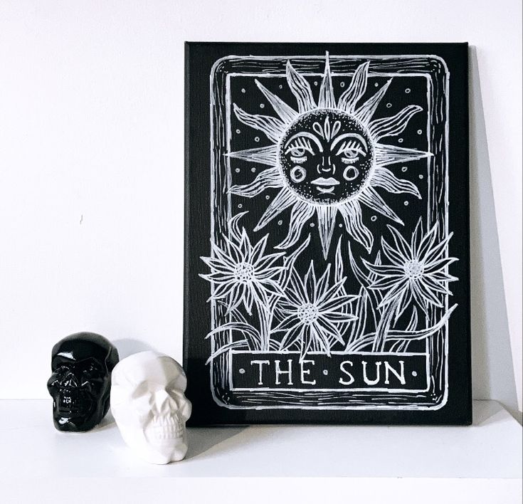 a white skull sitting next to a black and white tarot card with the sun on it