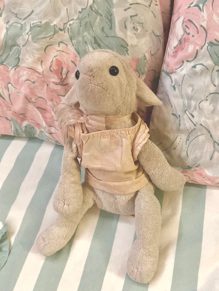 a stuffed animal sitting on top of a bed next to striped pillows and pink flowers