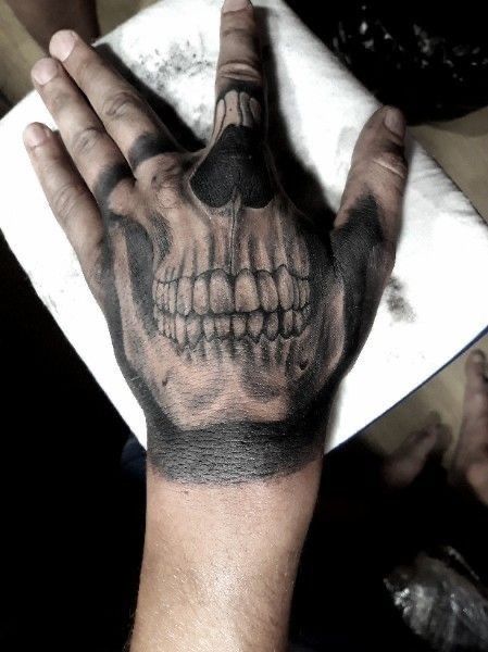 a hand with a skull on it holding something in the middle of its palm,