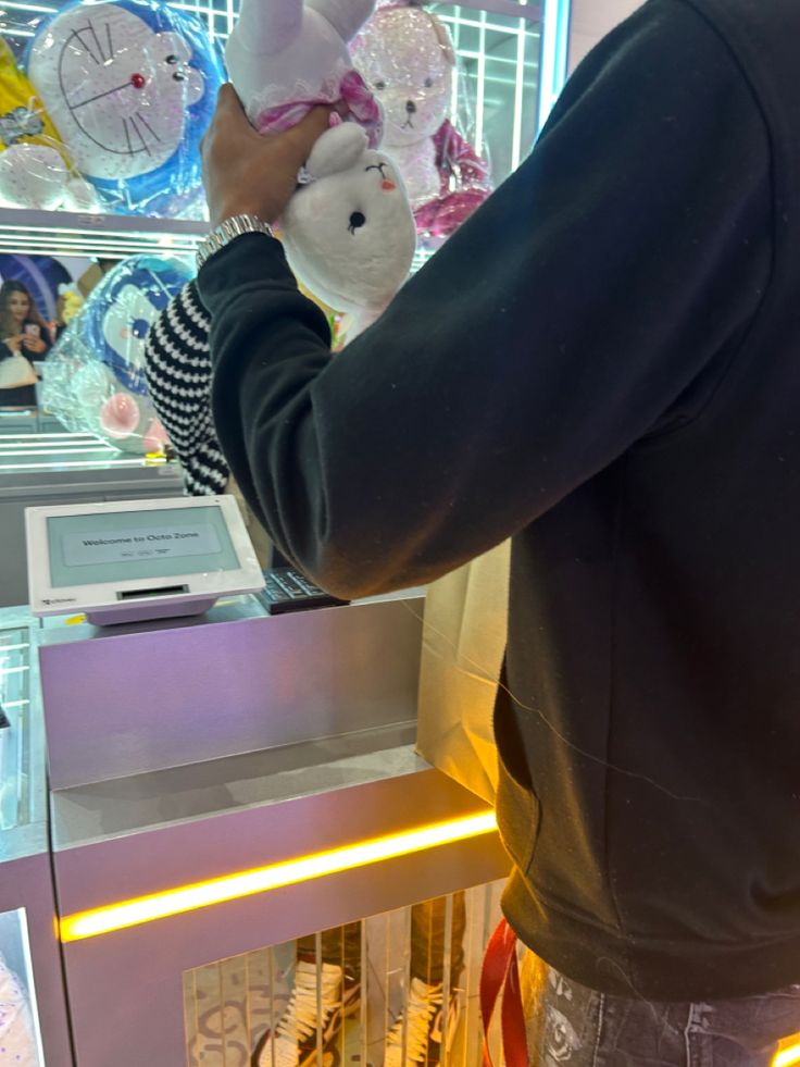 a man holding a stuffed animal in front of a display case with other items on it