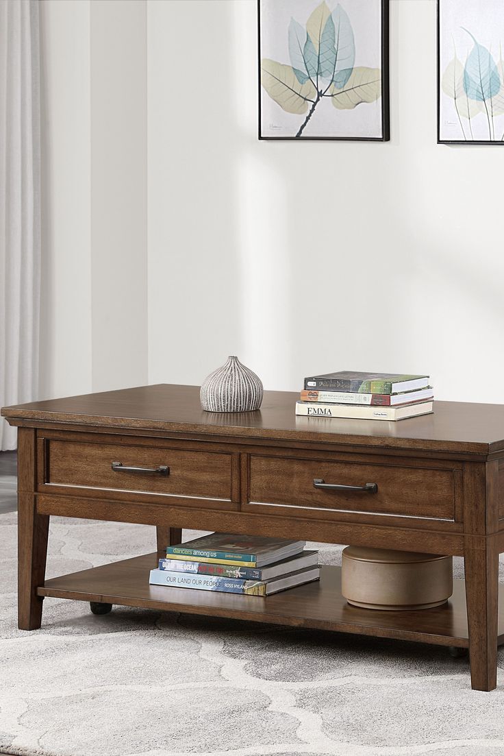 a wooden coffee table with two drawers on top and books on the bottom, in front of a white wall