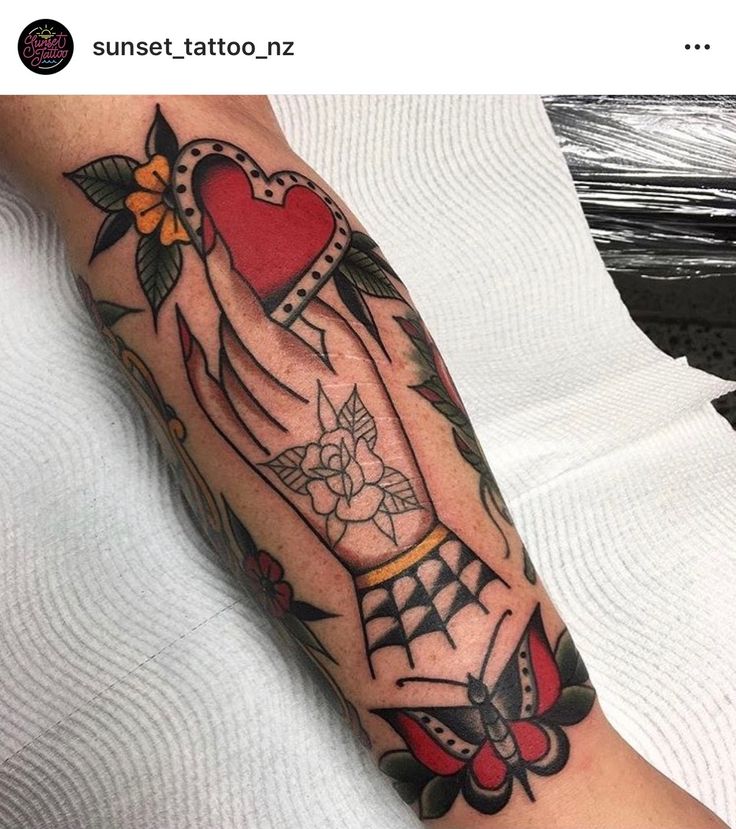 a person with a tattoo on their arm holding a red heart and an arrow in the middle