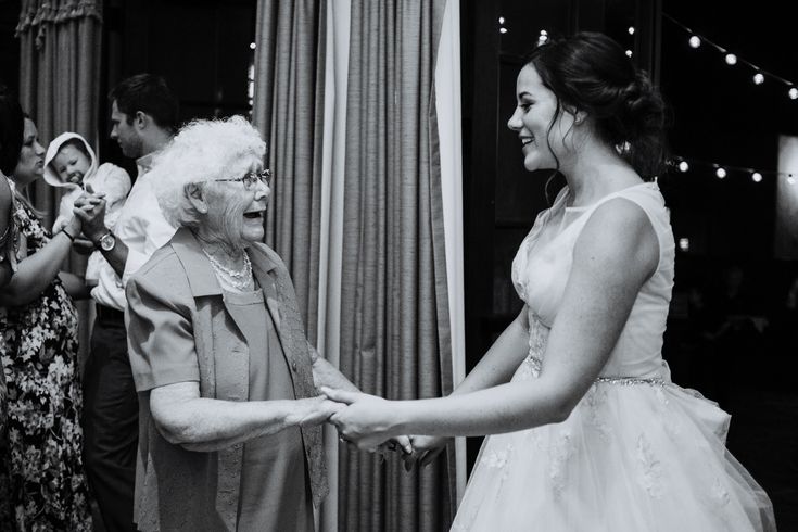 a woman in a wedding dress is shaking hands with an older lady on the dance floor