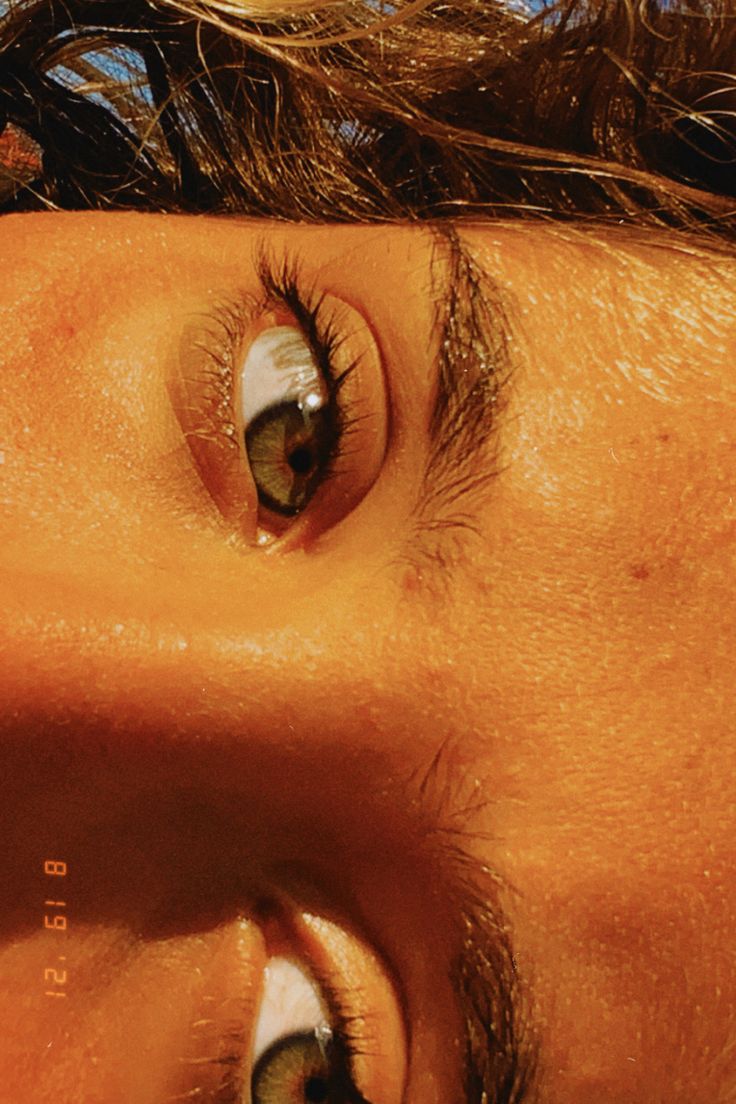 a close up of a person's face with brown hair and blue sky in the background