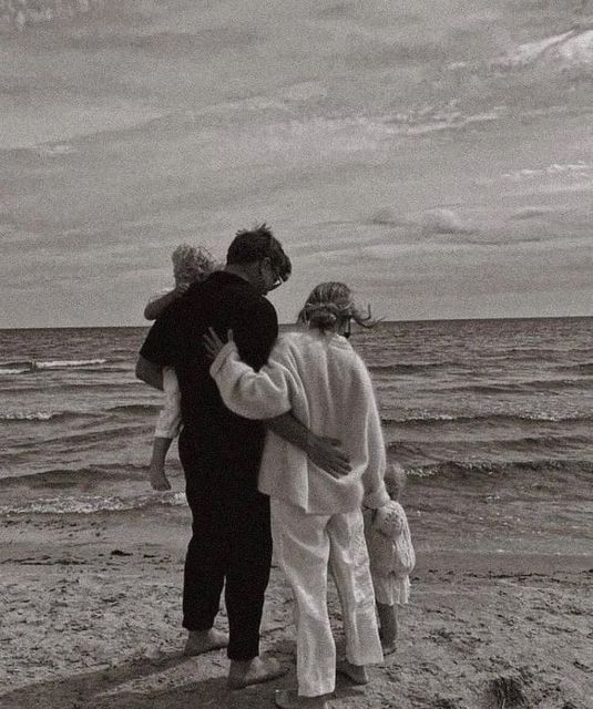 three people are standing on the beach with their arms around each other and looking out at the ocean