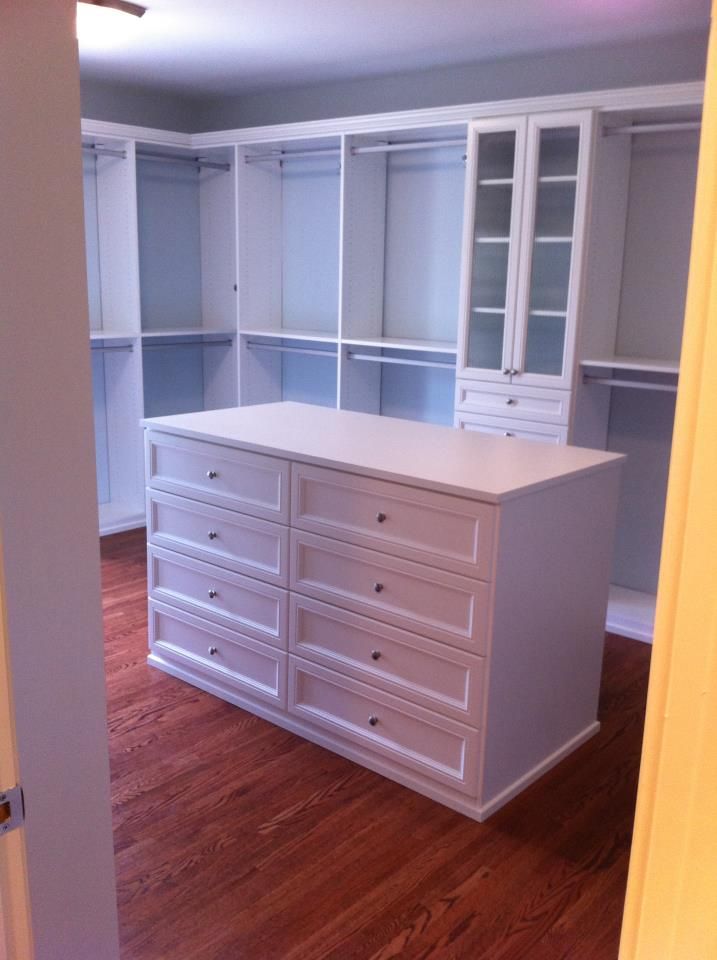 an empty room with white cabinets and drawers in the center, on hard wood flooring