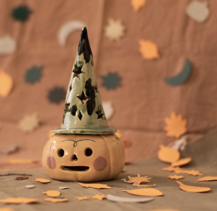 a ceramic pumpkin with a hat on it's head sitting on a table covered in confetti