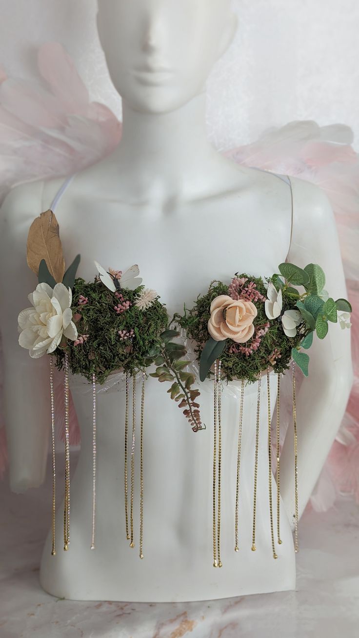 a white mannequin with flowers and greenery on it's chest, in front of a pink background