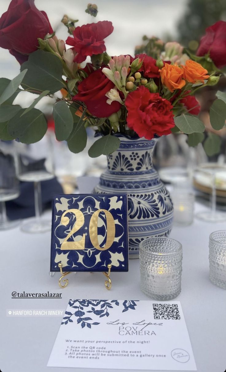 a blue vase with red and orange flowers in it next to a card that says 20th