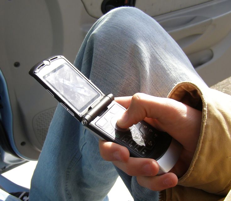 a person is holding a cell phone in their hand while sitting on the back of a car